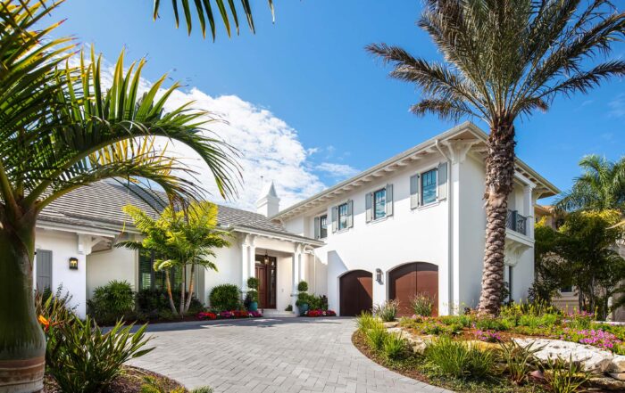 Two-story coastal residence with palm-lined drive, light exterior palette, and elevated massing suited for waterfront conditions