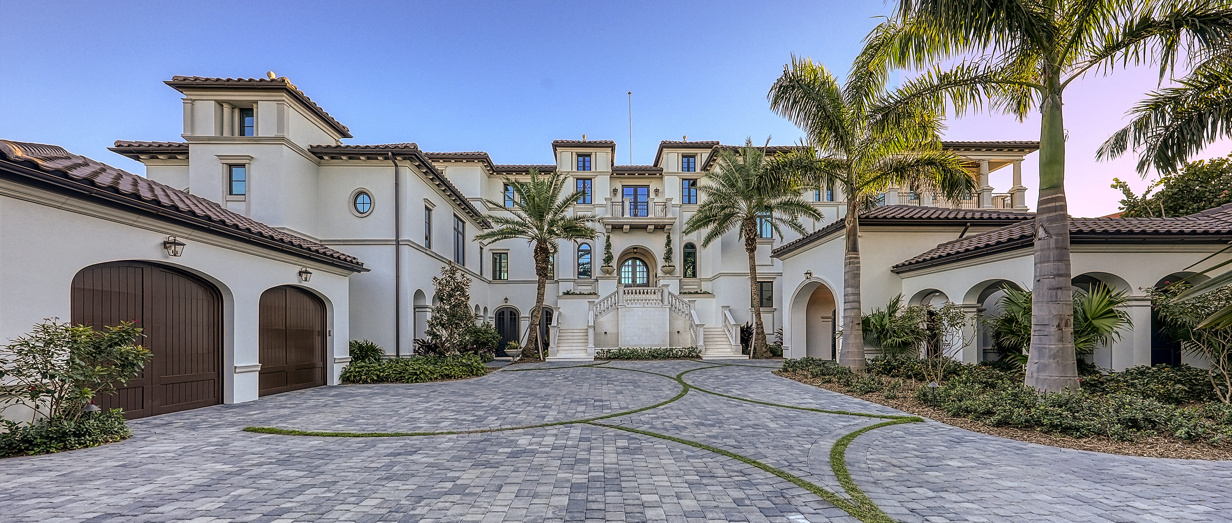 Grand Spanish Mediterranean-style estate in Sarasota designed by CMSA Architects, with stucco exterior, arched windows, red-tiled roof, and palm-lined driveway leading to an elegant entrance