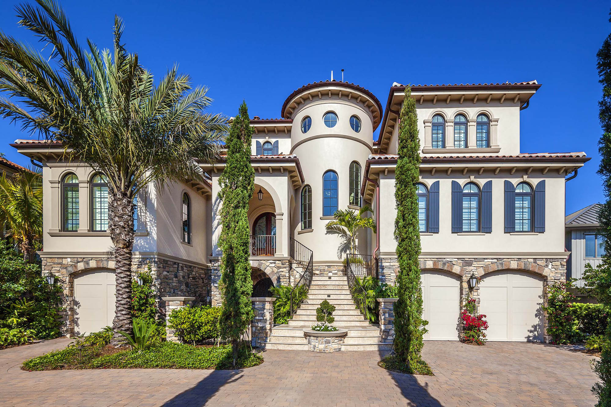 Mediterranean-style home façade with stone detailing, arched entry, and symmetrical massing