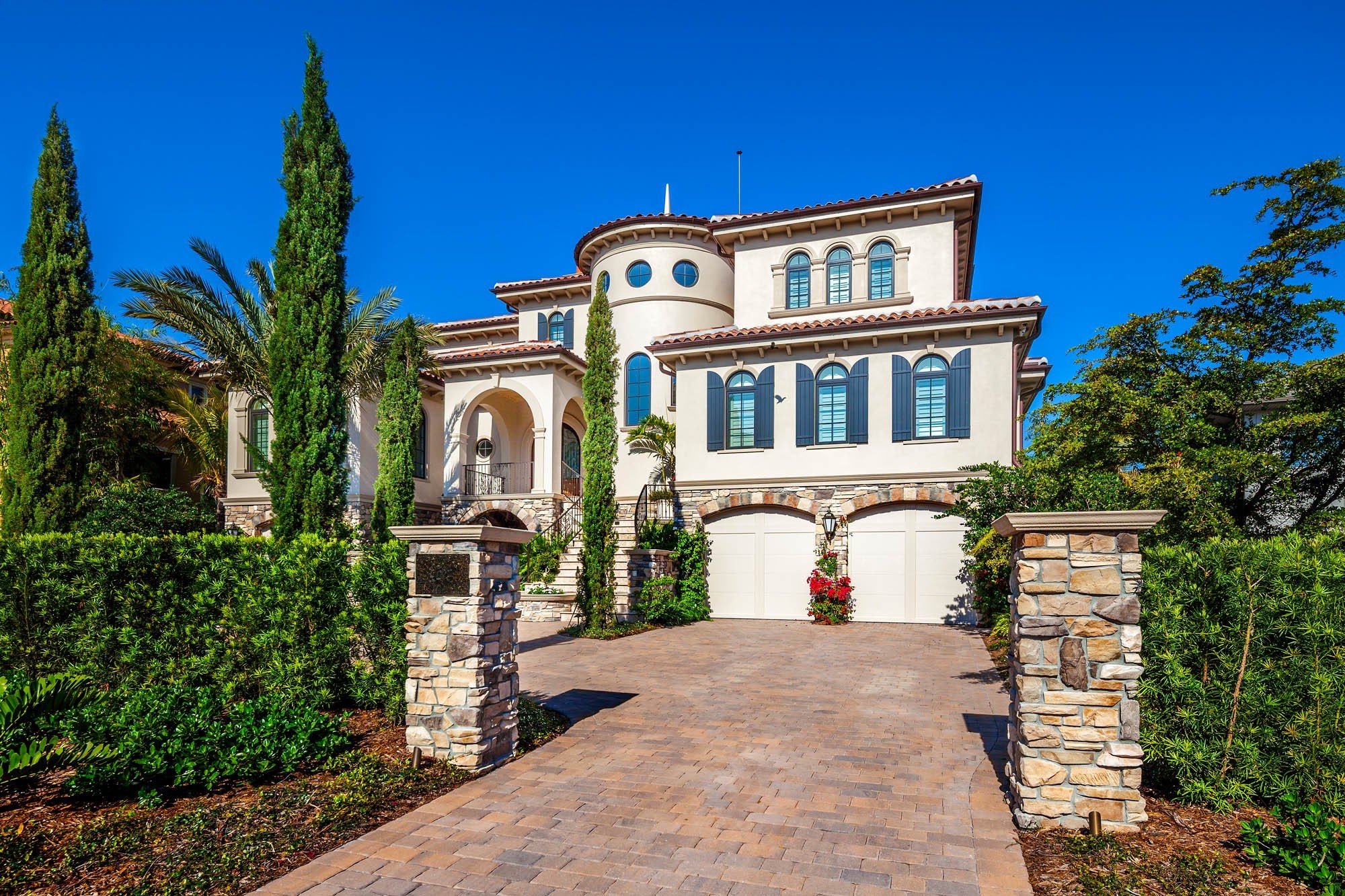 Formal motor court approach with Mediterranean architecture, stone walls, and mature landscaping